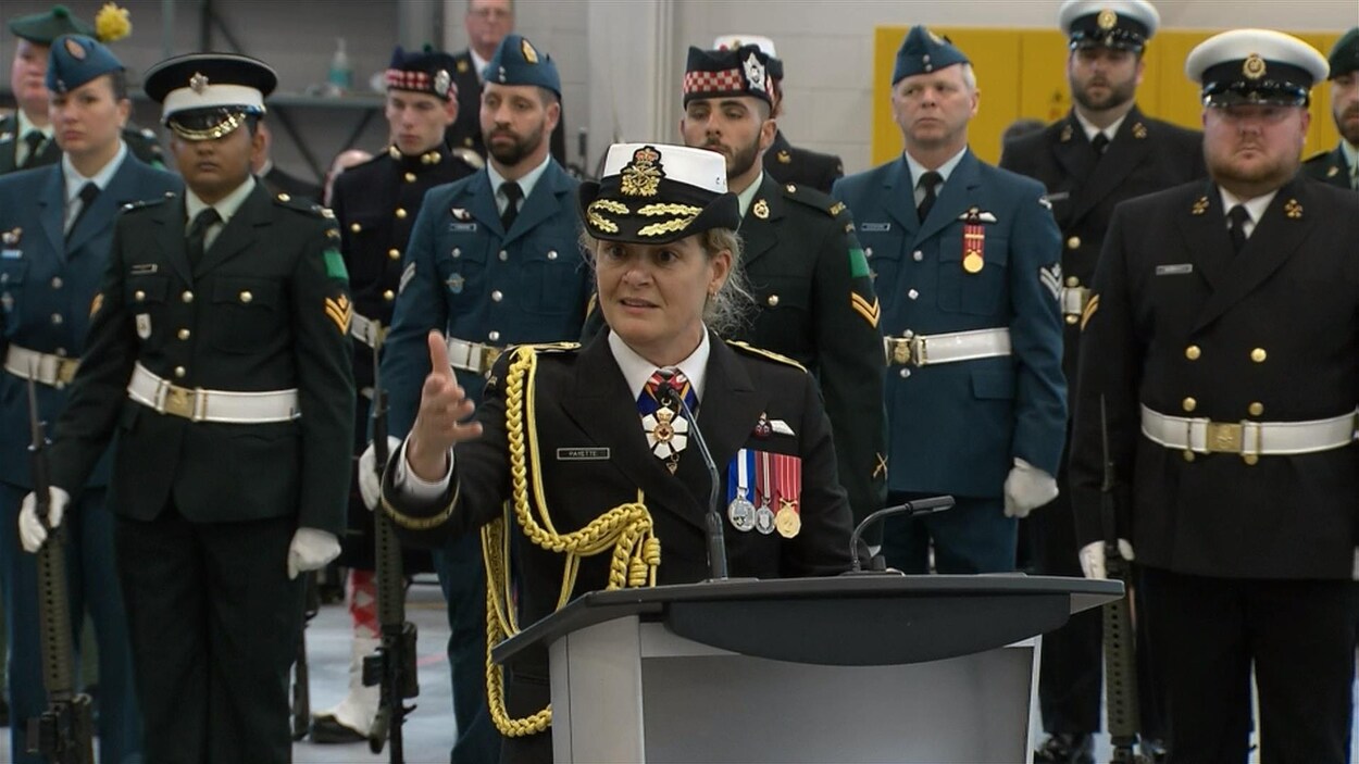 Julie Payette, en uniforme, parle au podium alors qu'on voit des militaires à l'arrière.