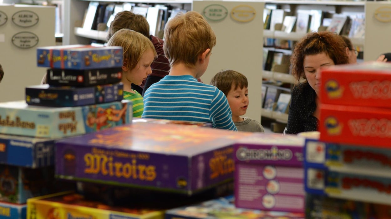 Des enfants jouent derrière des piles de boîtes de jeux de société.