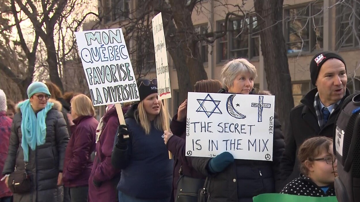 Des personnes portent des pancartes sur lesquelles est écrit : « Mon Québec favorise la diversité » et «The secret is in the mix », cette dernière accompagnée de dessins représentant une croix de David, un croissant et une étoile, ainsi qu'un crucifix.