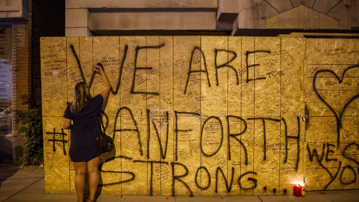 Une femme écrit un message de condoléances sur le mur d’un édifice après la fusillade de l’avenue Danforth.