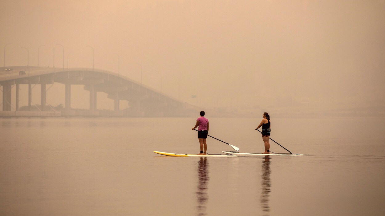 Deux pagayeuses circulent sur le lac Okanagan avec un épais brouillard autour d'elles.