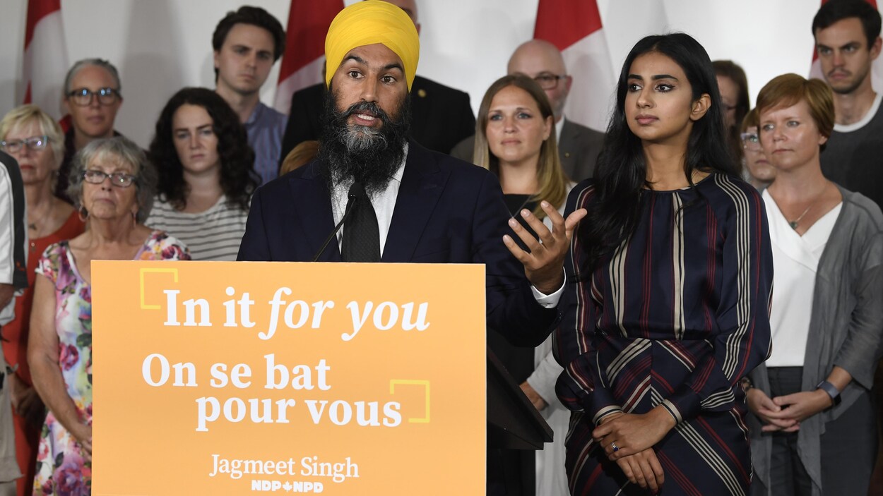 Un homme avec un turban est devant un lutrin aux couleurs de son parti où est inscrit : « On se bat pour vous. » Derrière lui se trouvent des hommes et des femmes de tous les âges.
