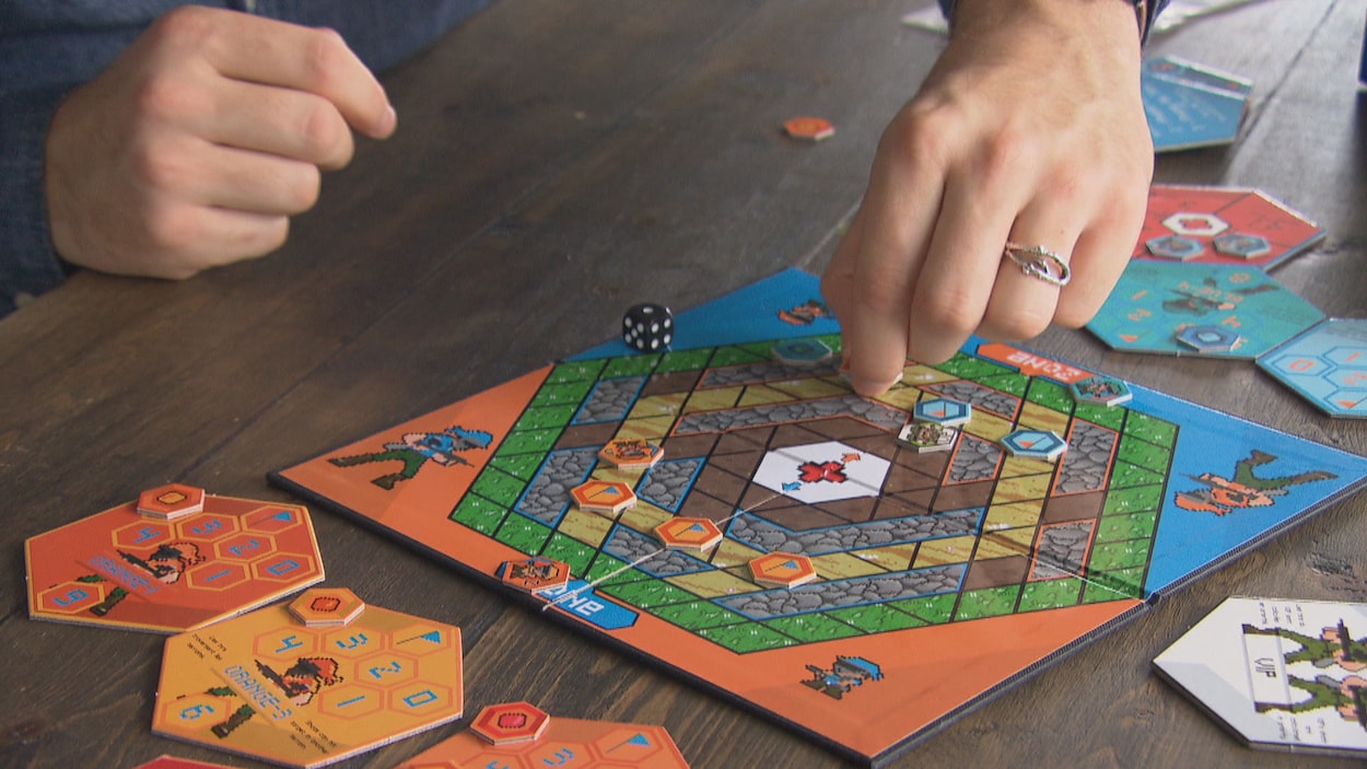 Une planche de jeu colorée disposée sur une table et des mains qui y jouent.