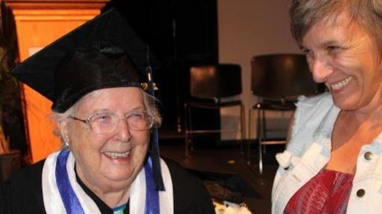 Une femme âgée habillée en toge tient son diplôme à côté d'une de ses enseignantes. Une femme âgée habillée en toge tient son diplôme à côté d'une de ses enseignantes.