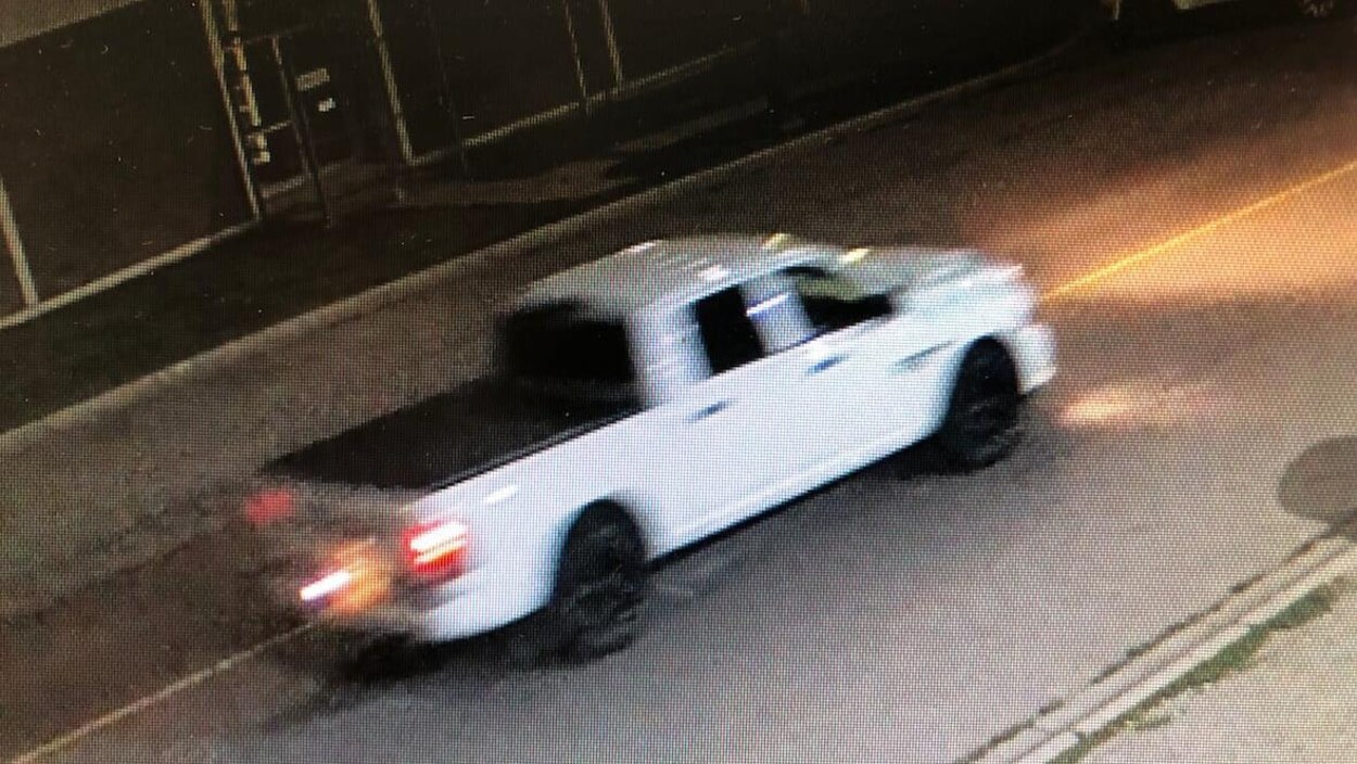 Une camionnette blanche circule dans la rue, le soir.