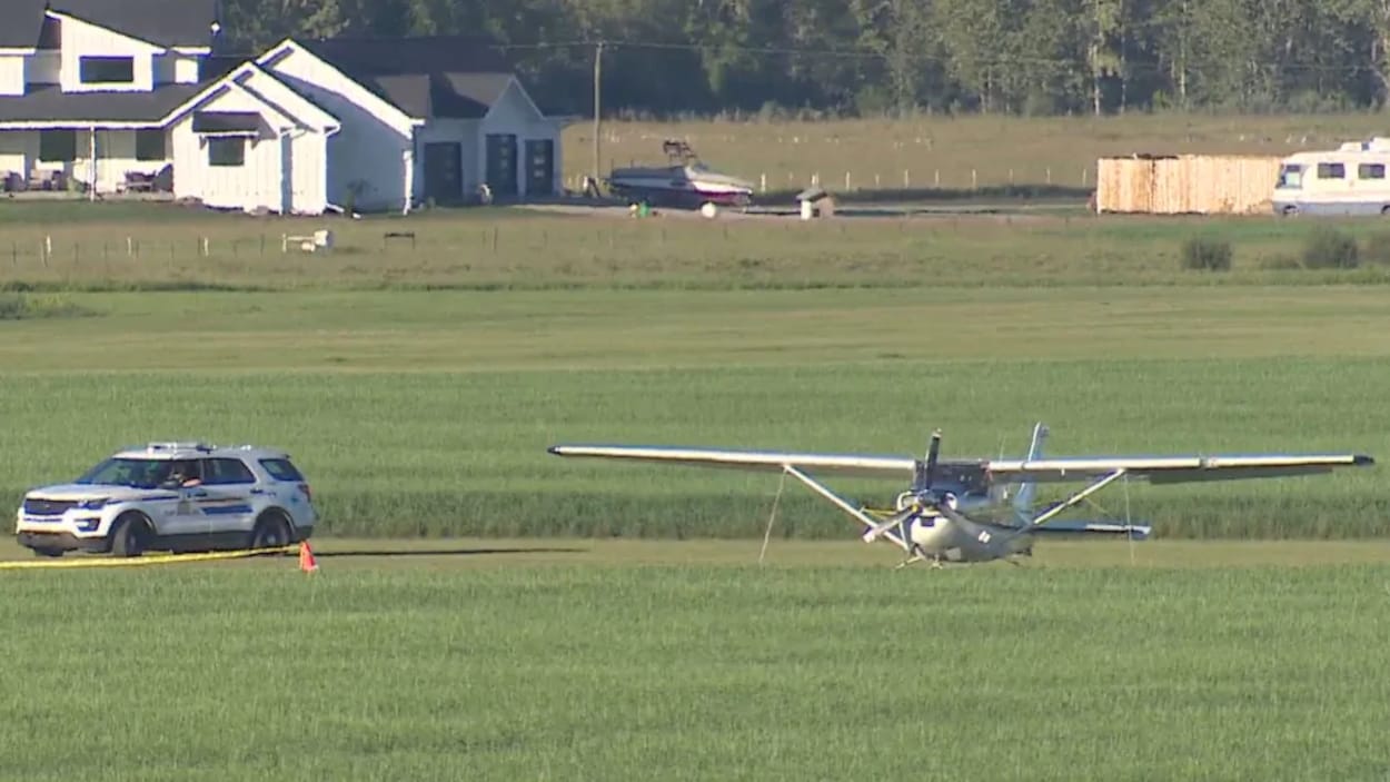 Un avion est posé dans un champ, à côté d'un véhicule utilitaire sport de la Gendarmerie royale du Canada.