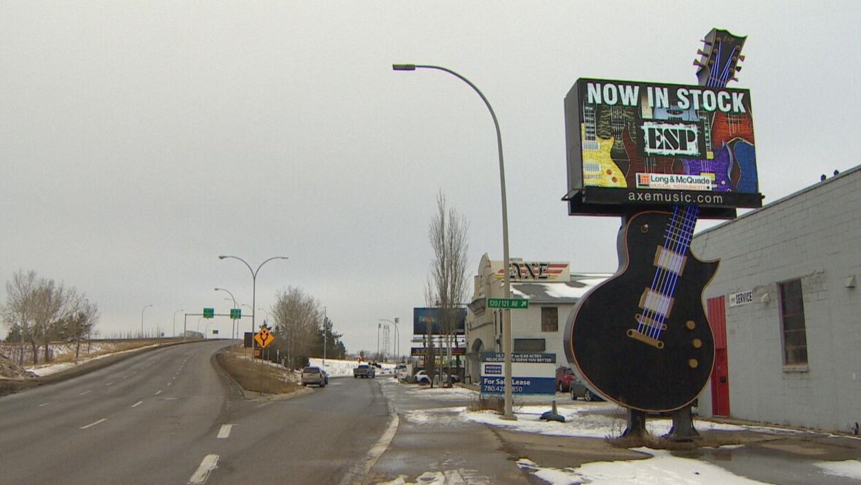 Une enseigne géante en forme de guitare dont les cordes sont formées de tubes fluorescents, au bord d'une rue, devant un commerce.