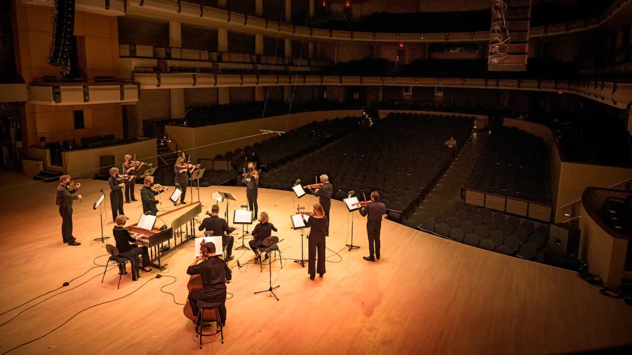 Des musiciens jouent sur une scène, devant une salle vide.