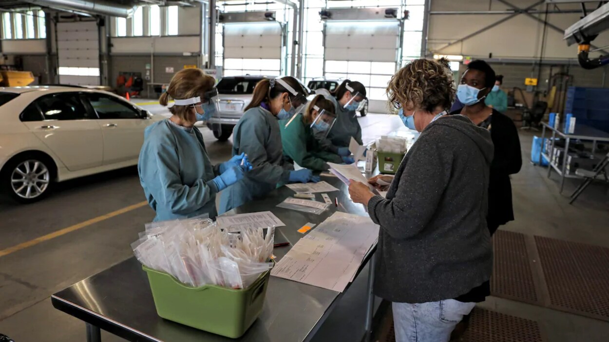 Du personnel médical regarde des papiers autour d'une table sur laquelle sont posés des ensembles de tests, dans un garage.