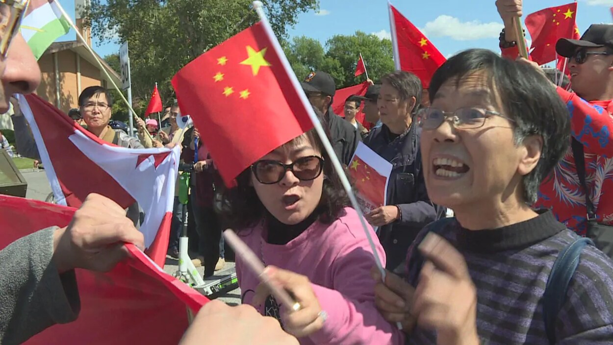 Une femme brandissant un drapeau chinois crie vers un autre manifestant dans une foule.