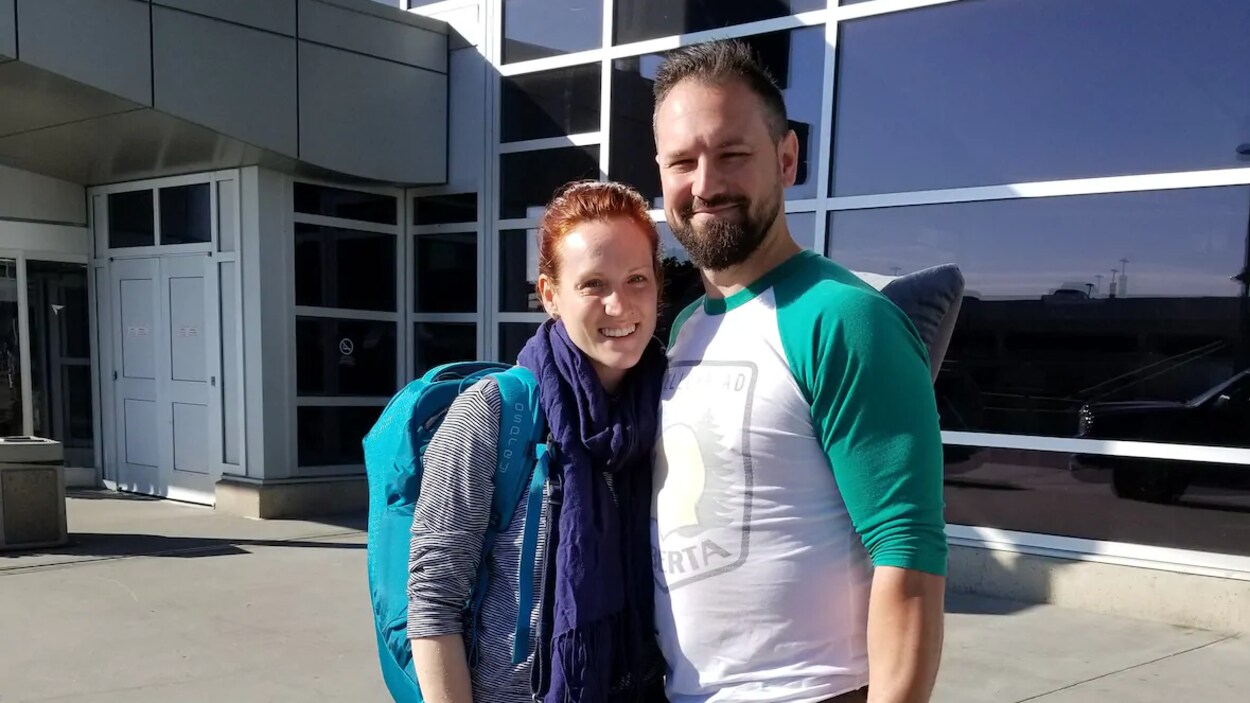 Un homme et une femme posent devant la porte d'un aéroport.