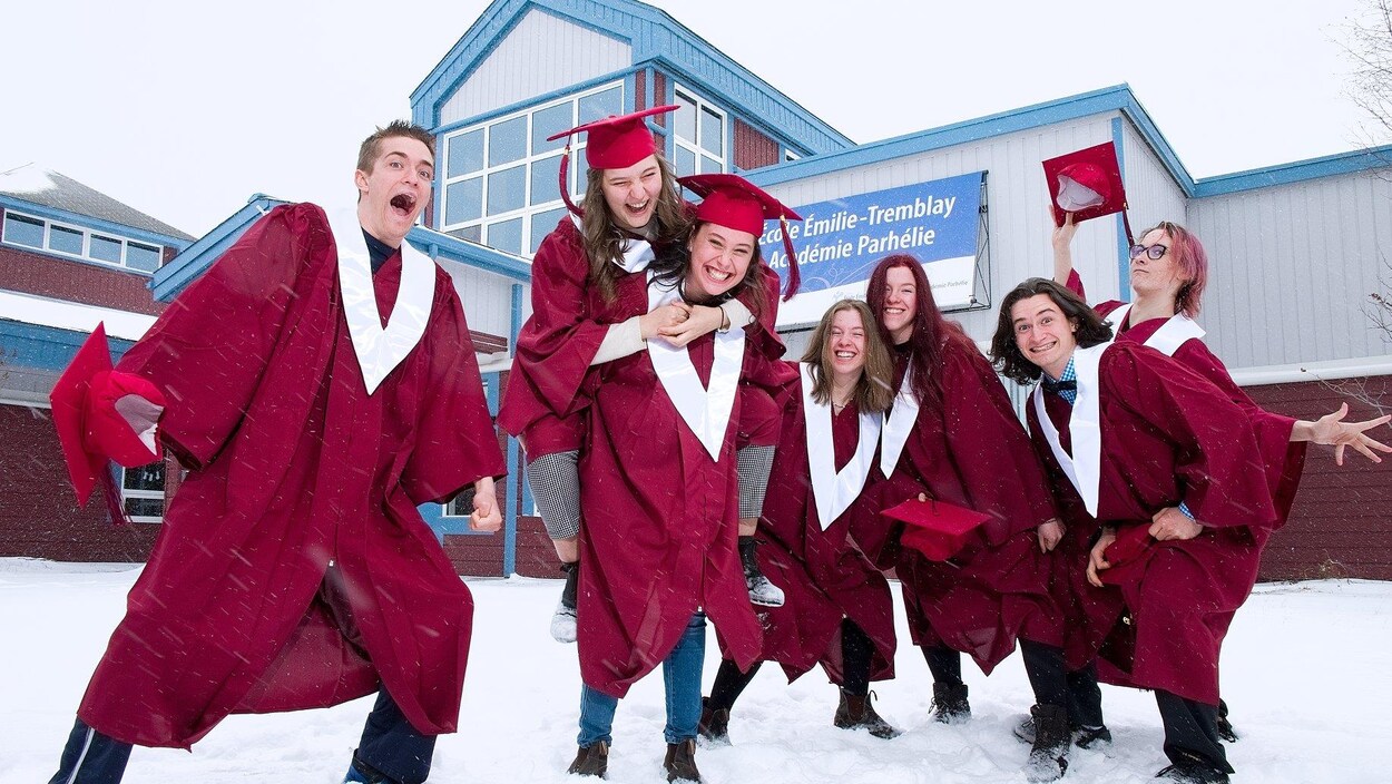 Les finissants en toge qui jouent dans la neige, devant leur école.