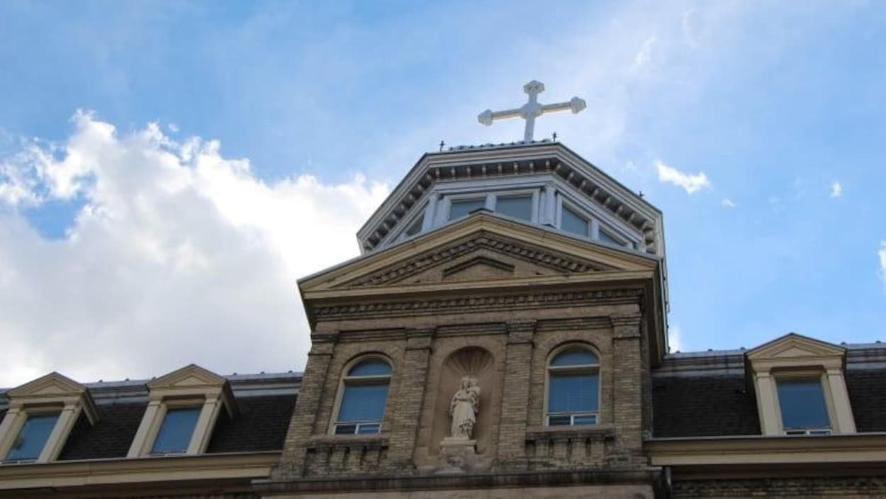 Le sommet d'un édifice avec une statue de la Vierge à l'engfant et une croix surplombant le toit.