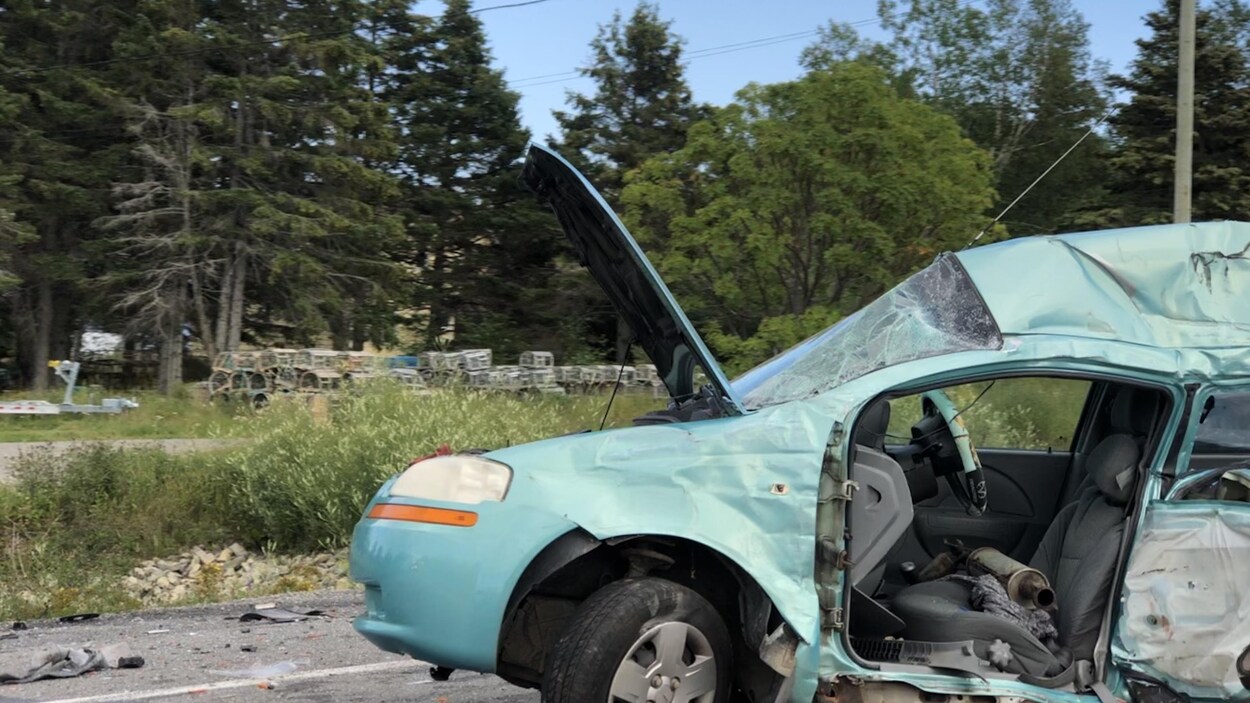 Un véhicule endommagé est immobilisé sur la route, le capot est ouvert. Le pare-brise est brisé en plusieurs morceaux.
