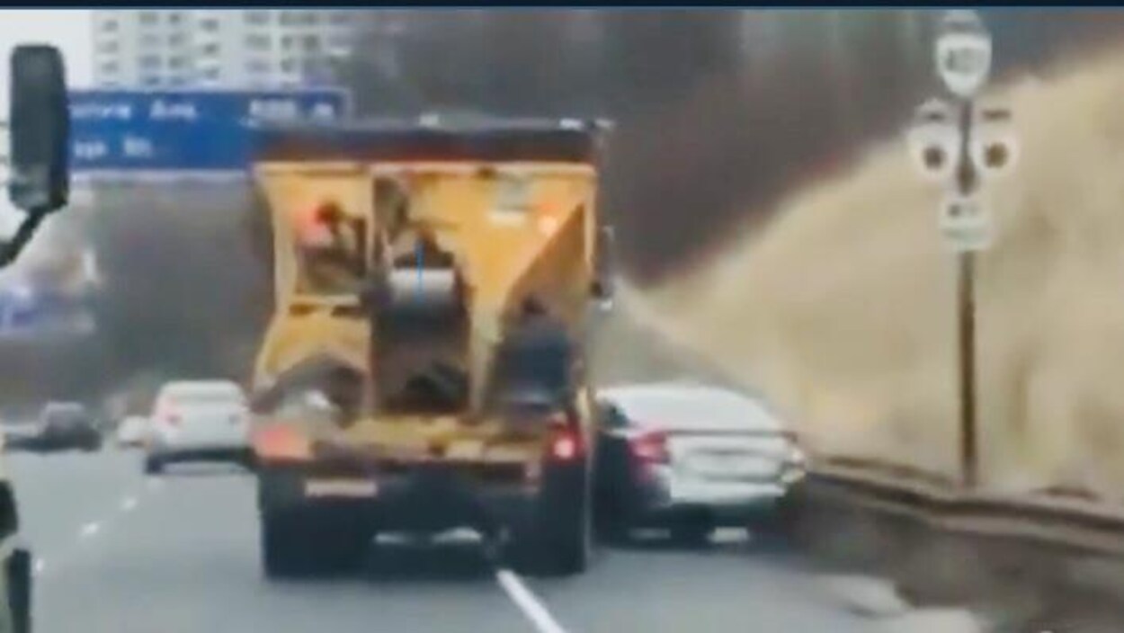 Un camion orange pousse une voiture grise sur chaussée.