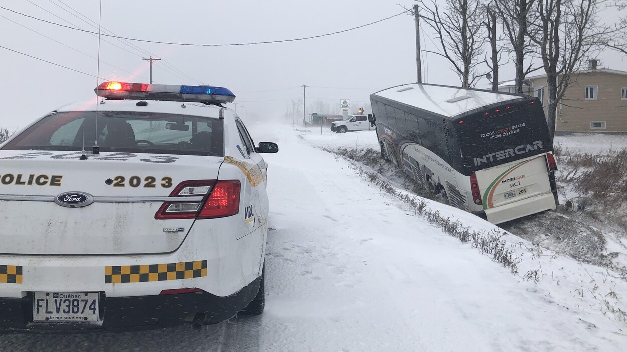 Un véhicule de police se trouve à proximité d'un autobus coincé dans un fossé.