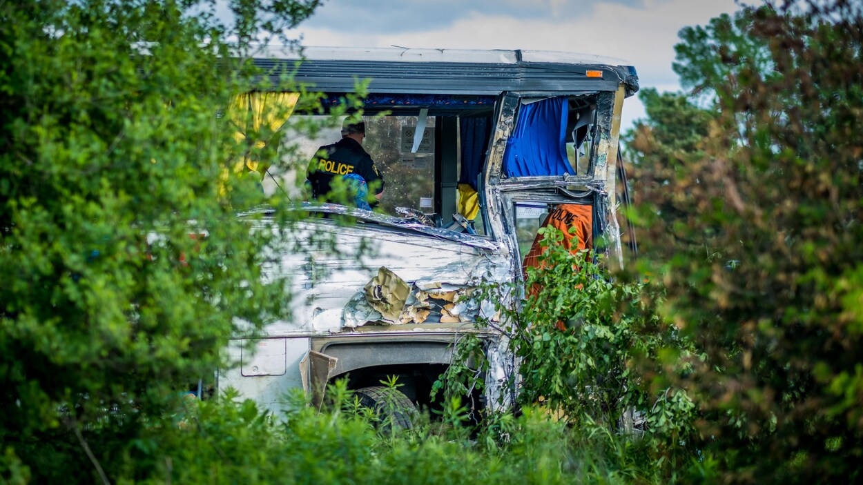 La façade d'un autocar accidenté en bordure de route. Un policier se trouve à l'intérieur du véhicule.