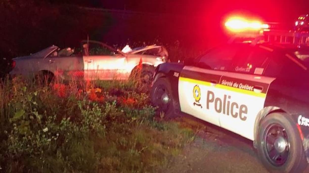 Une voiture accidentée devant laquelle se trouve une voiture de la Sûreté du Québec.
