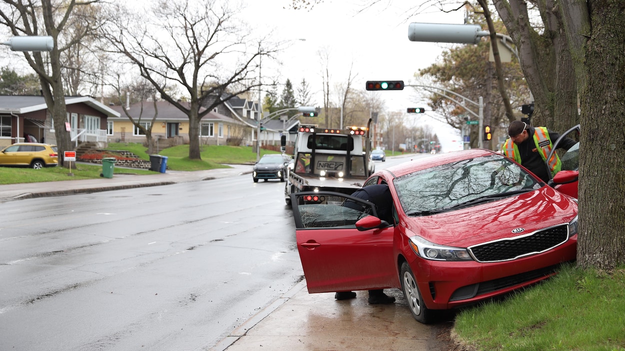Une voiture rouge de marque Kia est immobilisée après avoir percuté un arbre. L’opérateur d’une dépanneuse s’apprête à remorquer le véhicule.