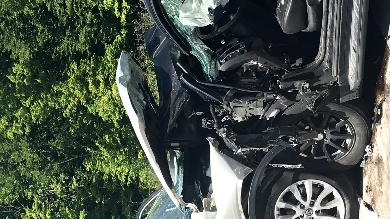 Une voiture blanche et une autre noire sont face à face. Le devant des deux voitures est complètement détruit. Une porte de la voiture noire a été arrachée.
