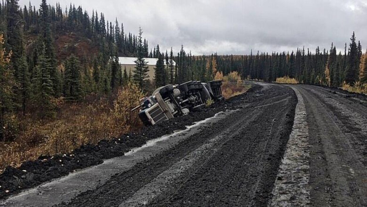 Une route en mauvais état et un camion renversé du côté gauche.