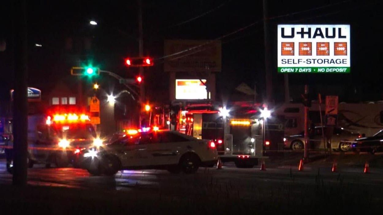 une voiture de police, un camion de pompier et un autre d'ambulancier stationnés près d'un périmètre de sécurité en pleine nuit
