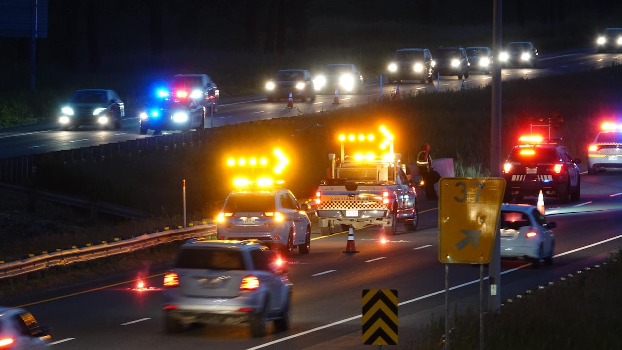 Une voie de circulation est fermée et des véhicules de police délimitent la circulation.