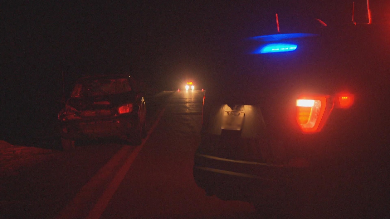 Une voiture de la Sûreté du Québec près d'un véhicule accidenté sur une route la nuit.