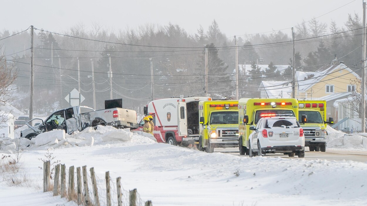 Un camion accidenté est monté sur un banc de neige, plusieurs véhicules d'urgence sont tout près, sur une route enneigée.