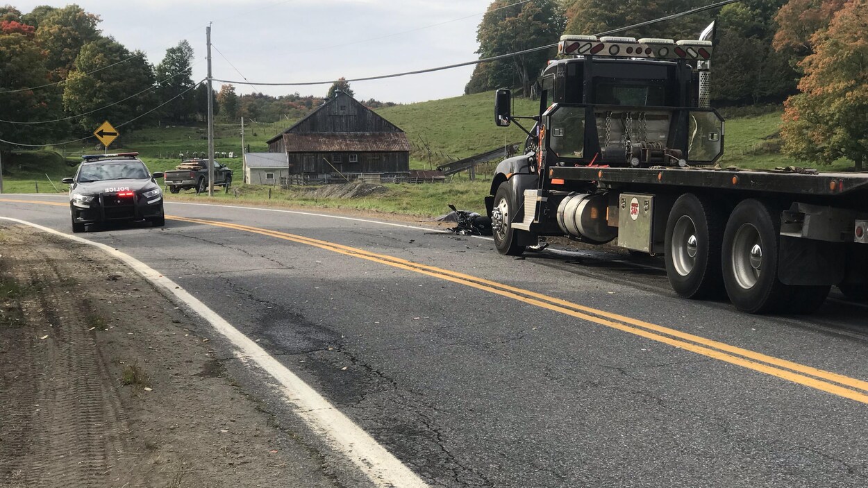 Une moto repose sur la route devant un camion remorque.