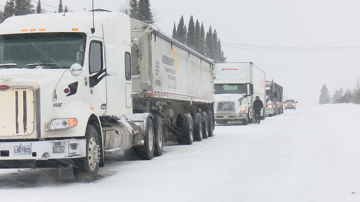 Des camions lourds sont immobilisés sur une route, à la queue leu leu.