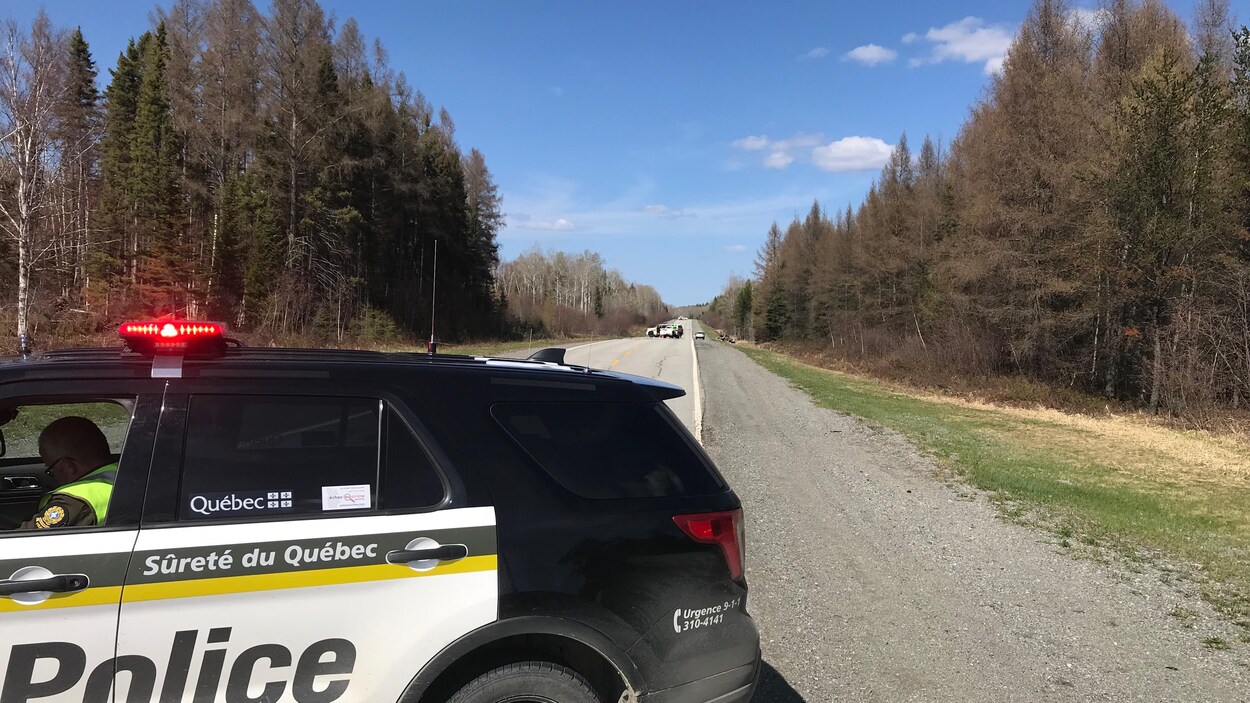 Une voiture de police bloque la route à quelques mètres d'une scène d'accident.