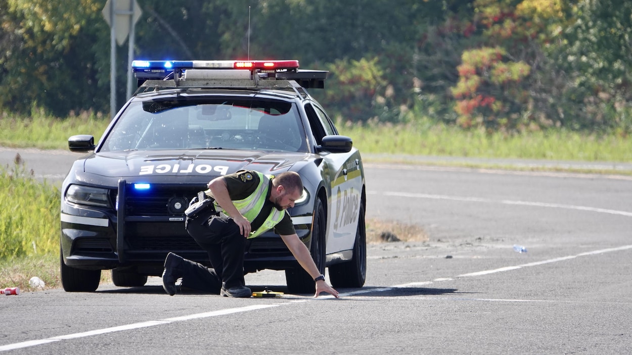 Un policier examine des traces sur la route après un accident.
