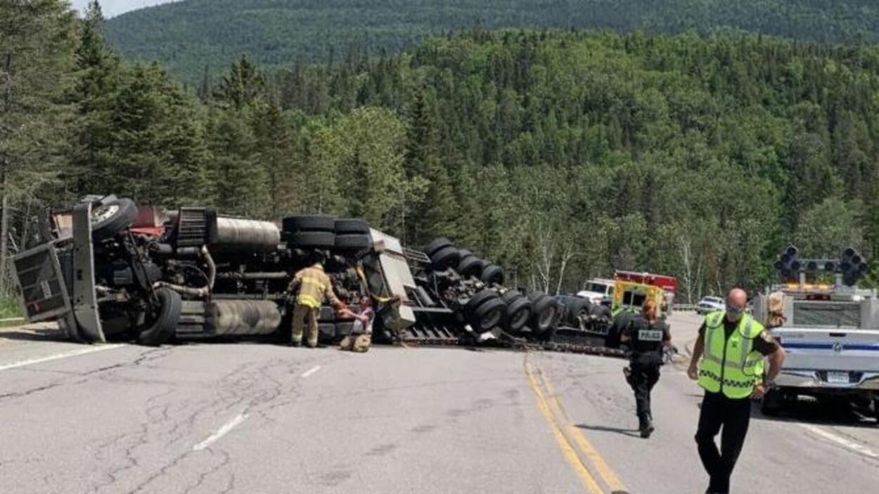 Un camion renversé sur la chaussée avec des secouristes autour.