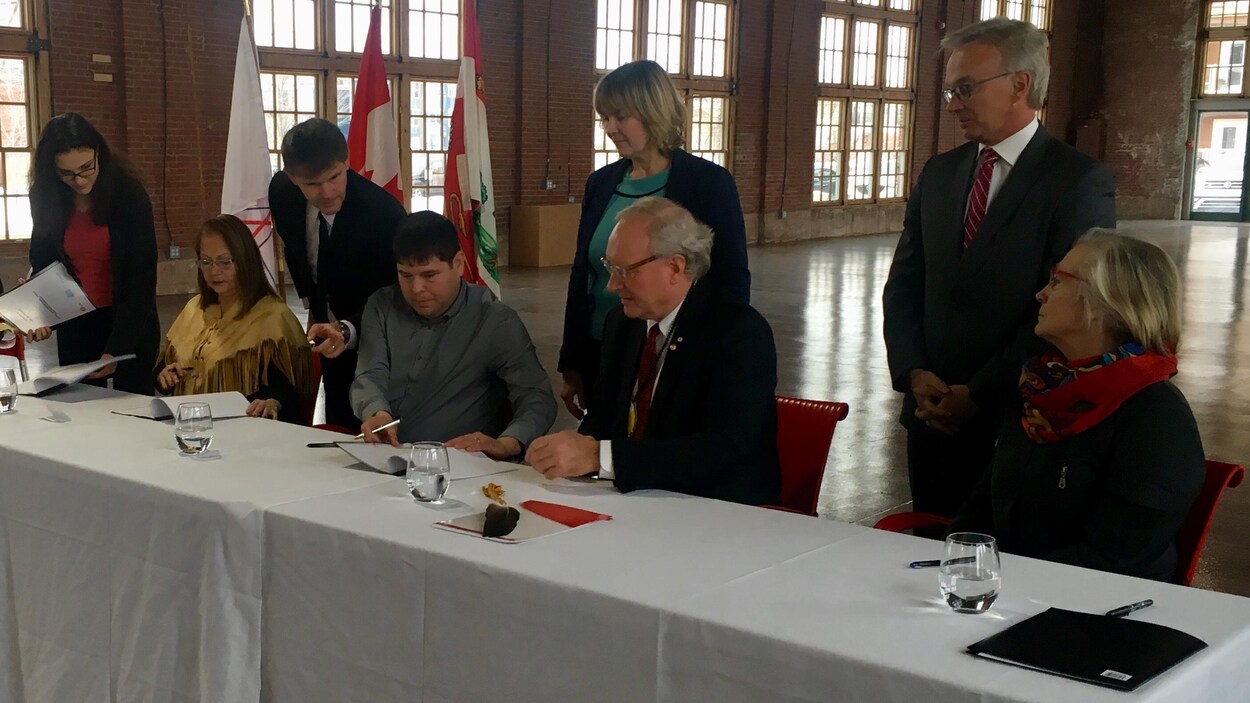 Des femmes et des hommes assis à une table signent un document.