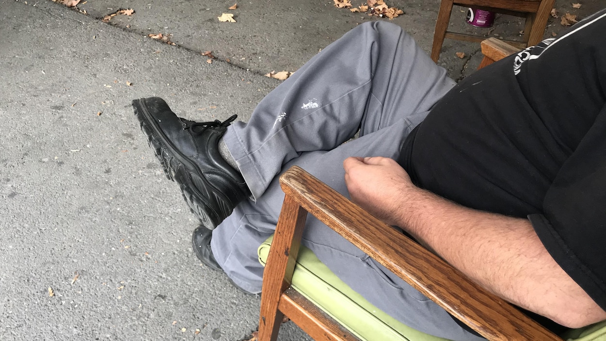 Un sans-abri dont on ne voit pas le visage est assis sur une chaise à l'extérieur.