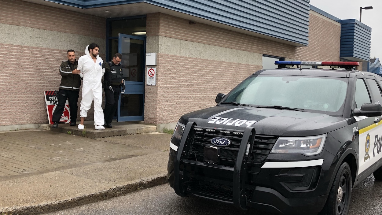 Un homme menotté est encadré par deux policiers.