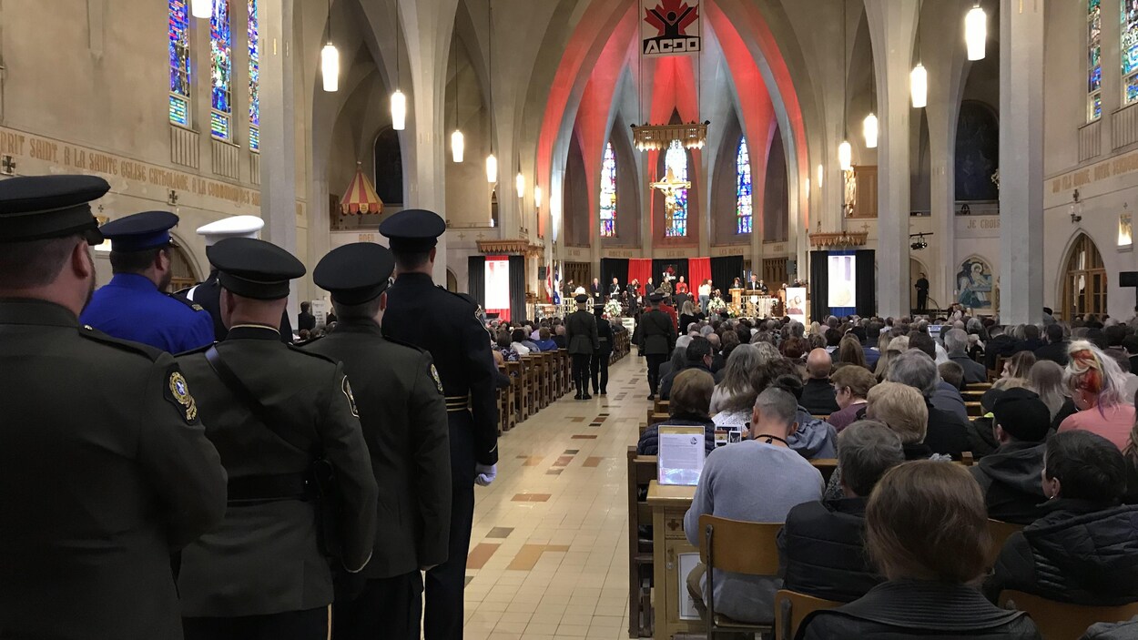 Des personnes assises dans la cathédrale de Sherbrooke. À l'arrière, des militaires attendent de faire leur entrée.