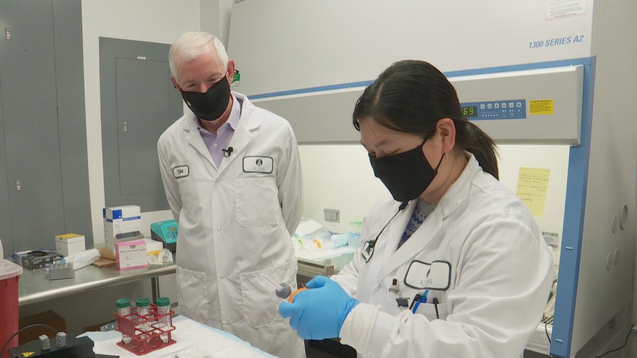 Deux personnes portant des masques sont en blouse blanche dans un laboratoire.