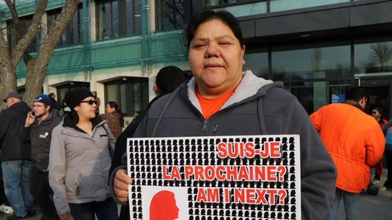 Une femme manifeste devant le palais de justice de Val-d'Or. Elle tient une pancarte sur laquelle on peut lire : « Suis-je la prochaine? Am I next? »