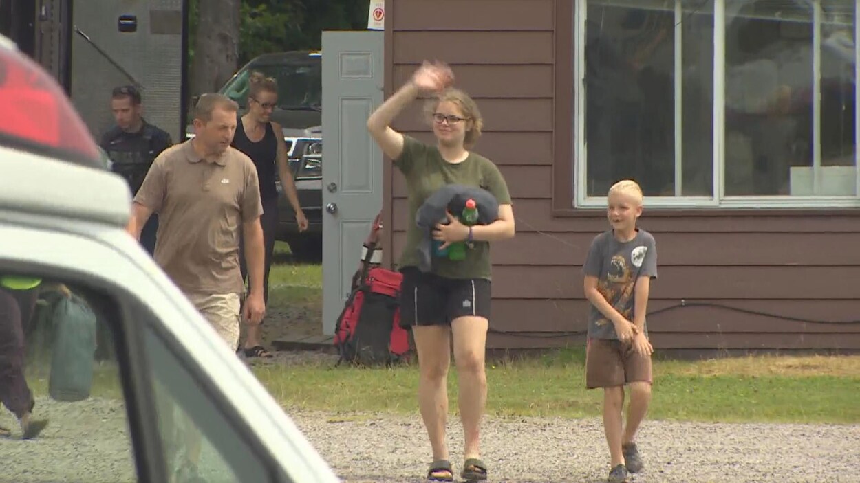 Une adolescente entourée de sa famille salue d'un signe de la main.
