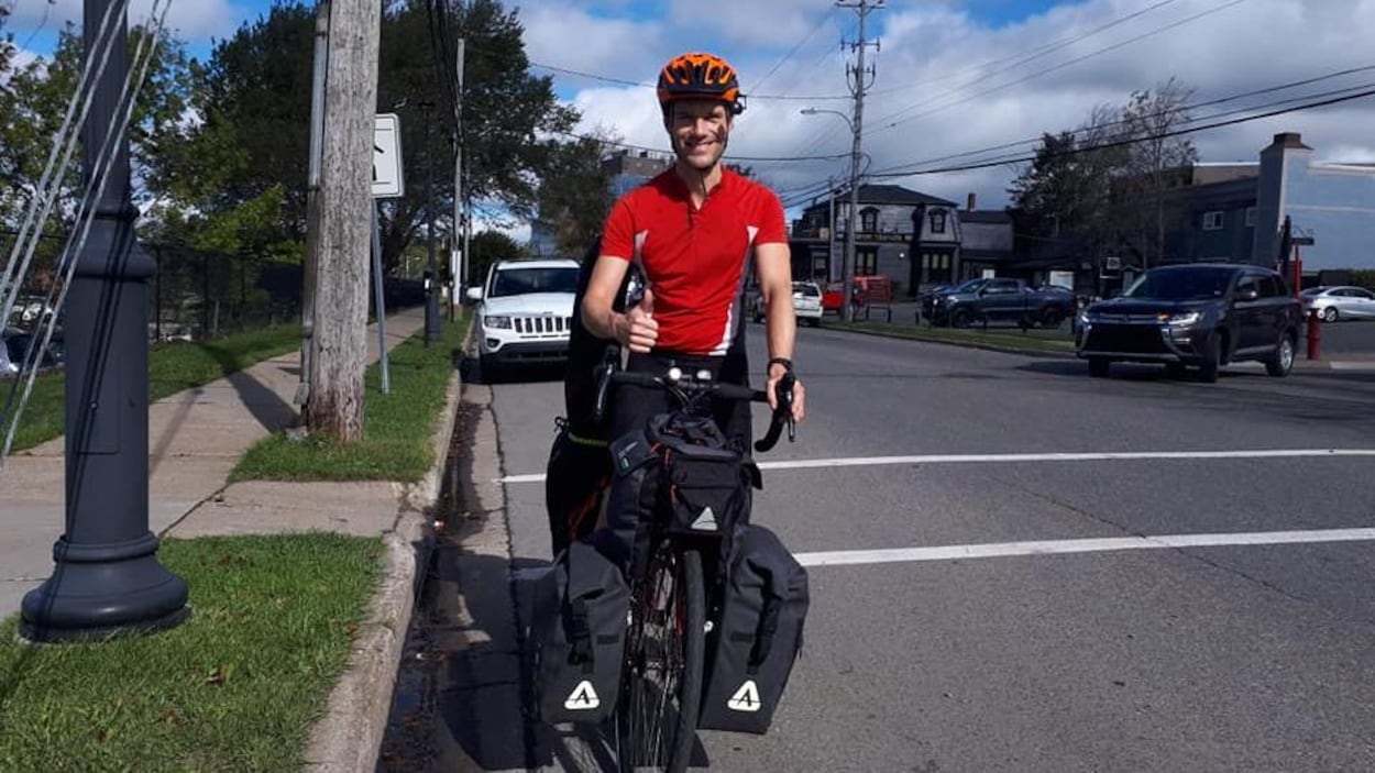 Adrian House sur sa bicyclette dans une rue résidentielle faisant un signe d'approbation du pouce.