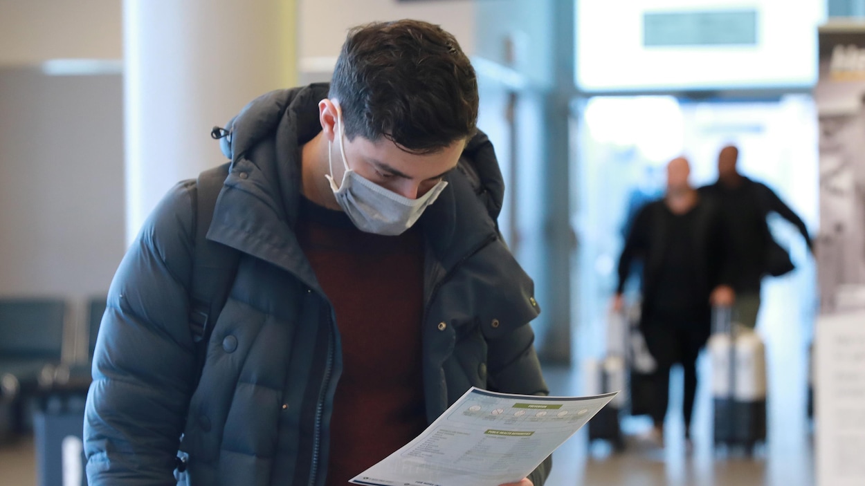 À son arrivée à l'aéroport Billy Bishop de Toronto, un voyageur consulte un dépliant de santé concernant la COVID-19.