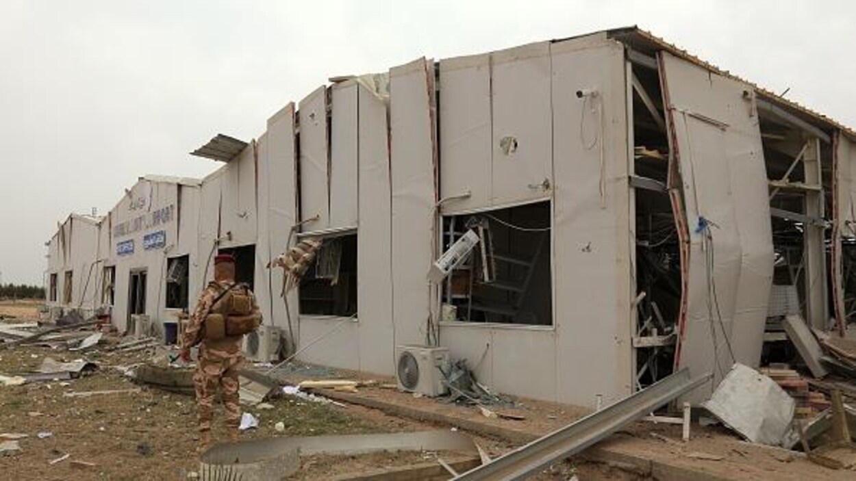Un soldat debout devant un bâtiment endommagé,