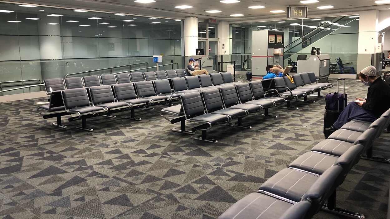 Trois personnes sont assises sur les sièges situés près d'une porte d'embarquement.
