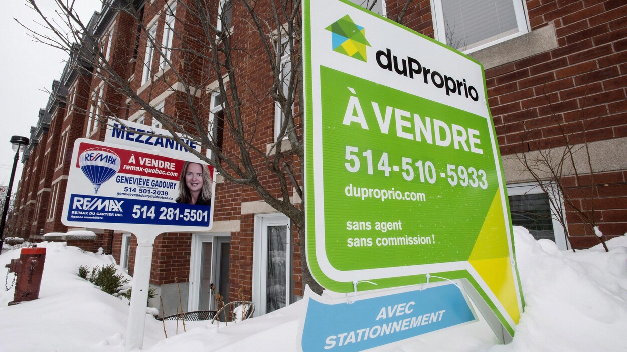 Deux affiches de condos à vendre devant un immeuble, à Montréal.