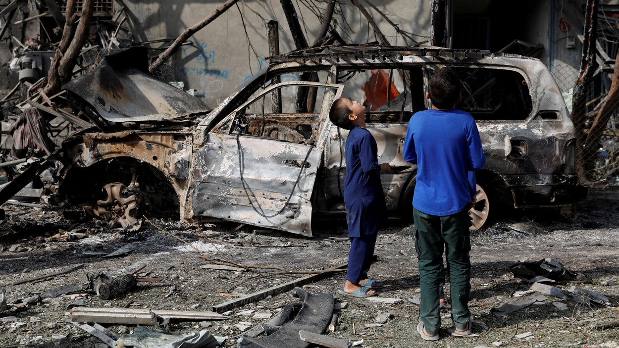Des enfants devant une voiture calcinée et un immeuble endommagé par une explosion terroriste.