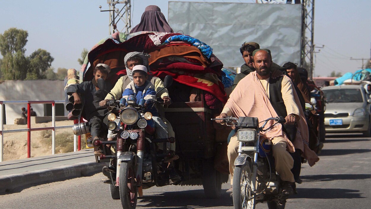 Des Afghans conduisent des motos sur une route. L'une tire une remorque bourrée d'effets personnels.