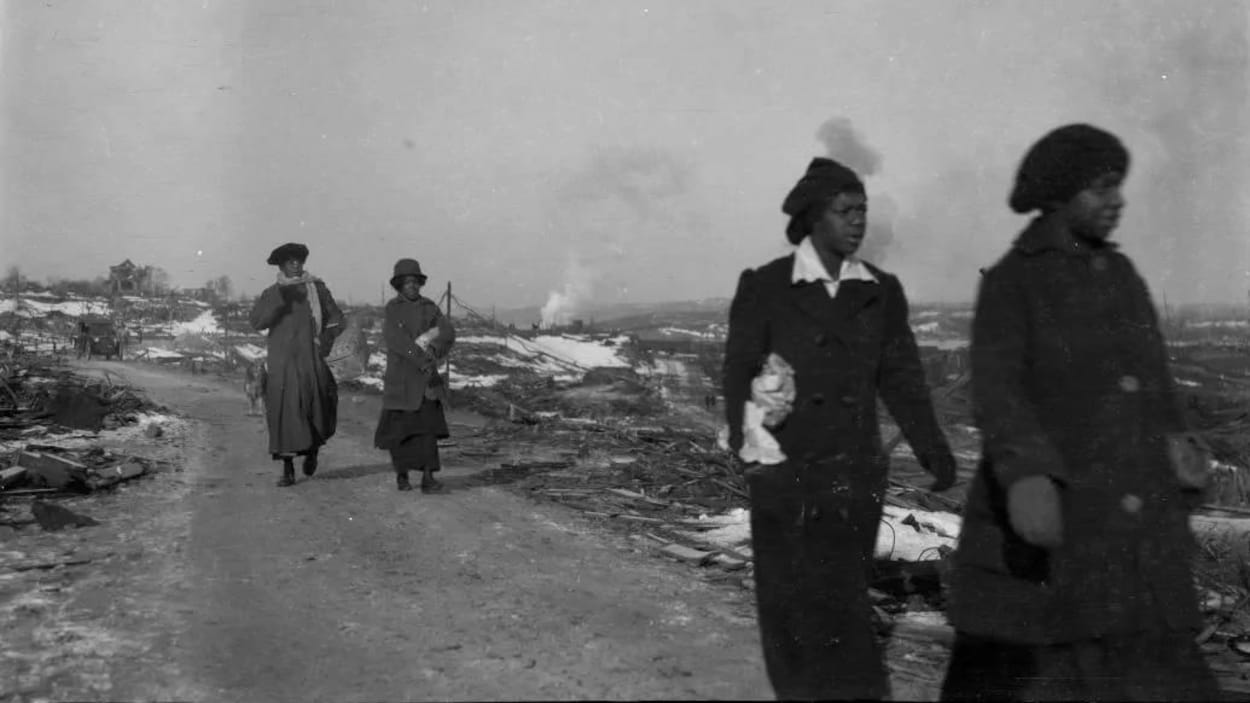 Photo en noir et blanc de quatre femmes vêtues de manteaux d'hiver avec la fumée de l'explosion dans le lointain.