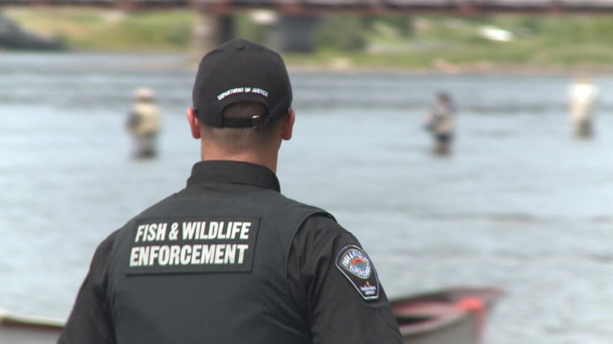 Un agent de pêche, vu de dos, regarde des pêcheurs dans une rivière. Un agent de pêche, vu de dos, regarde des pêcheurs dans une rivière.